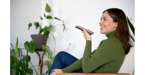 Person using voice assistant and smartphone to control smart light switch for home automation